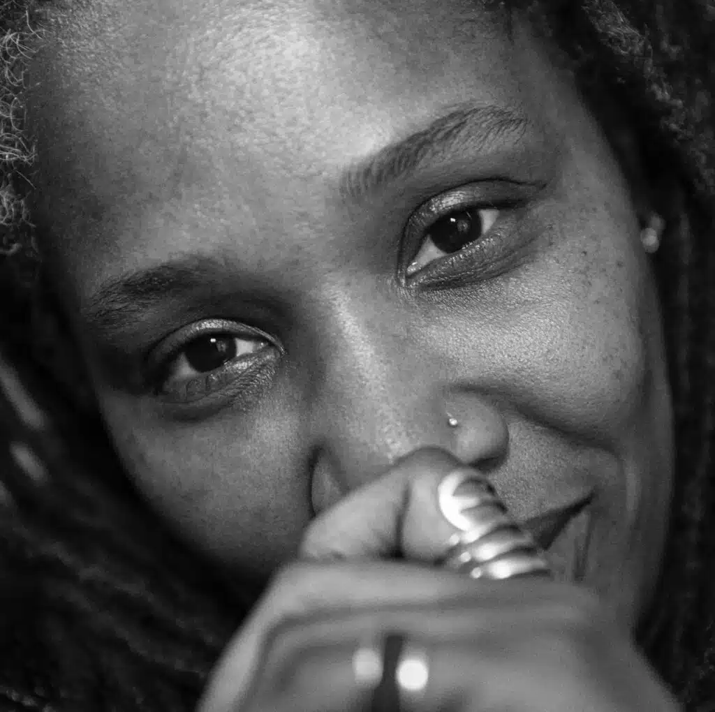black and white close up image of Marai Larasi, a Black person with locs looking directly at the camera