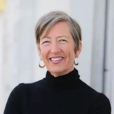 headshot of Staci Haines, a white woman with short grey hair wearing a black polo neck