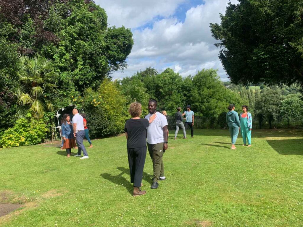 pairs of people stand in a green outdoor space facing each other with a hand extended towards another