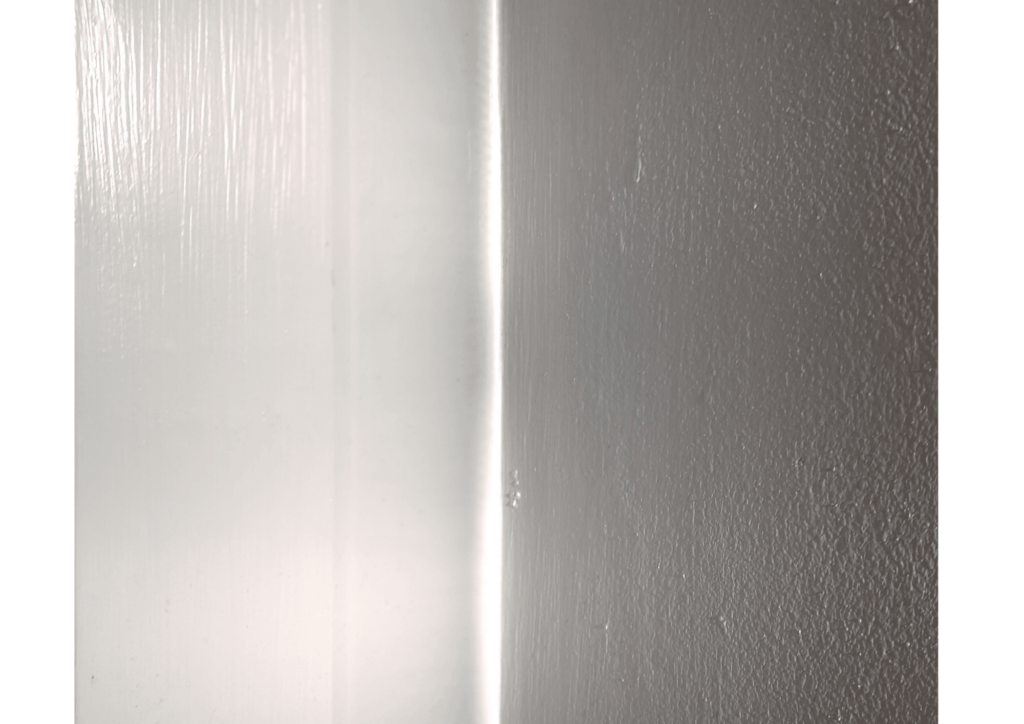 Photo of a white painted wall divided by sunlight that makes the left side appear brighter than the right, which is more grey
