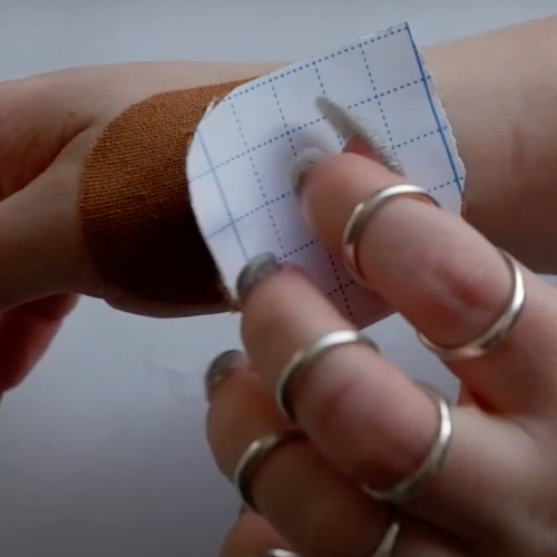 A hand with silver stabiliser rings places a plaster onto their other hand